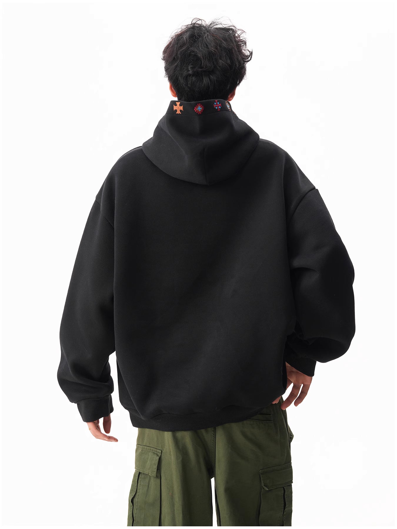 Person wearing a black hoodie with colorful designs on the hood, standing against a white background.