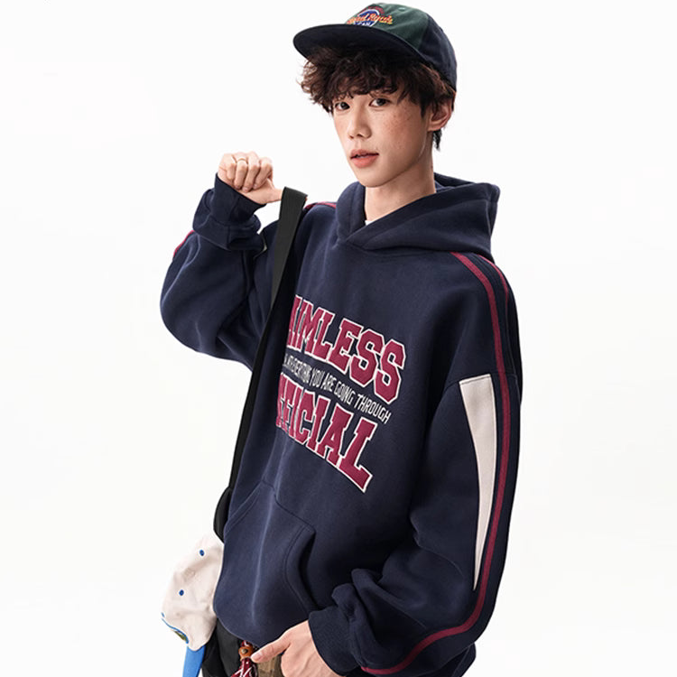 Person wearing a navy hoodie with red text, holding a plush toy and a bag, on a white background.